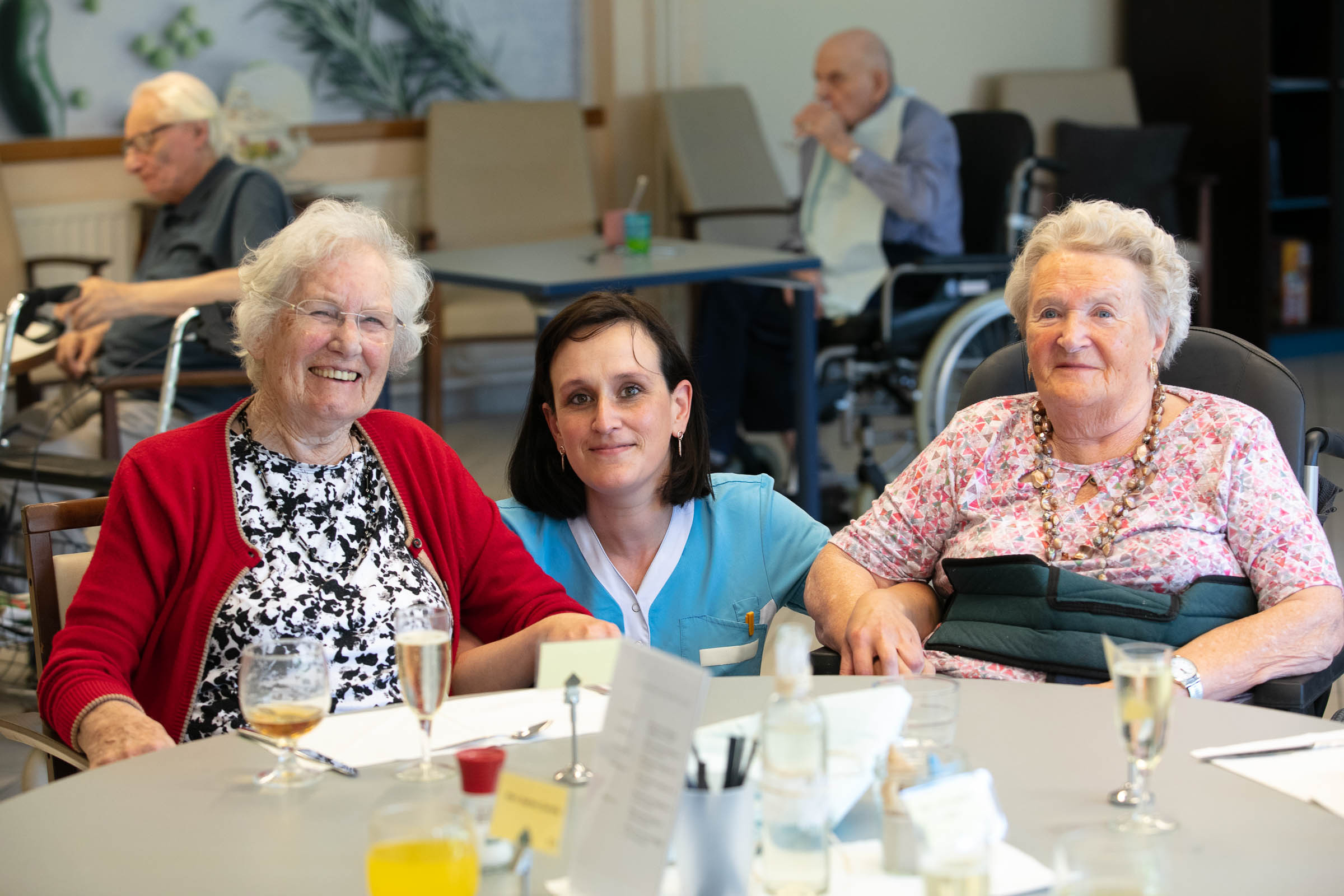 Seniorenzorg Philippus Neri twee senior bewoonsters met personeelslid in eetruimte Huize Den Dries in Sinaai
