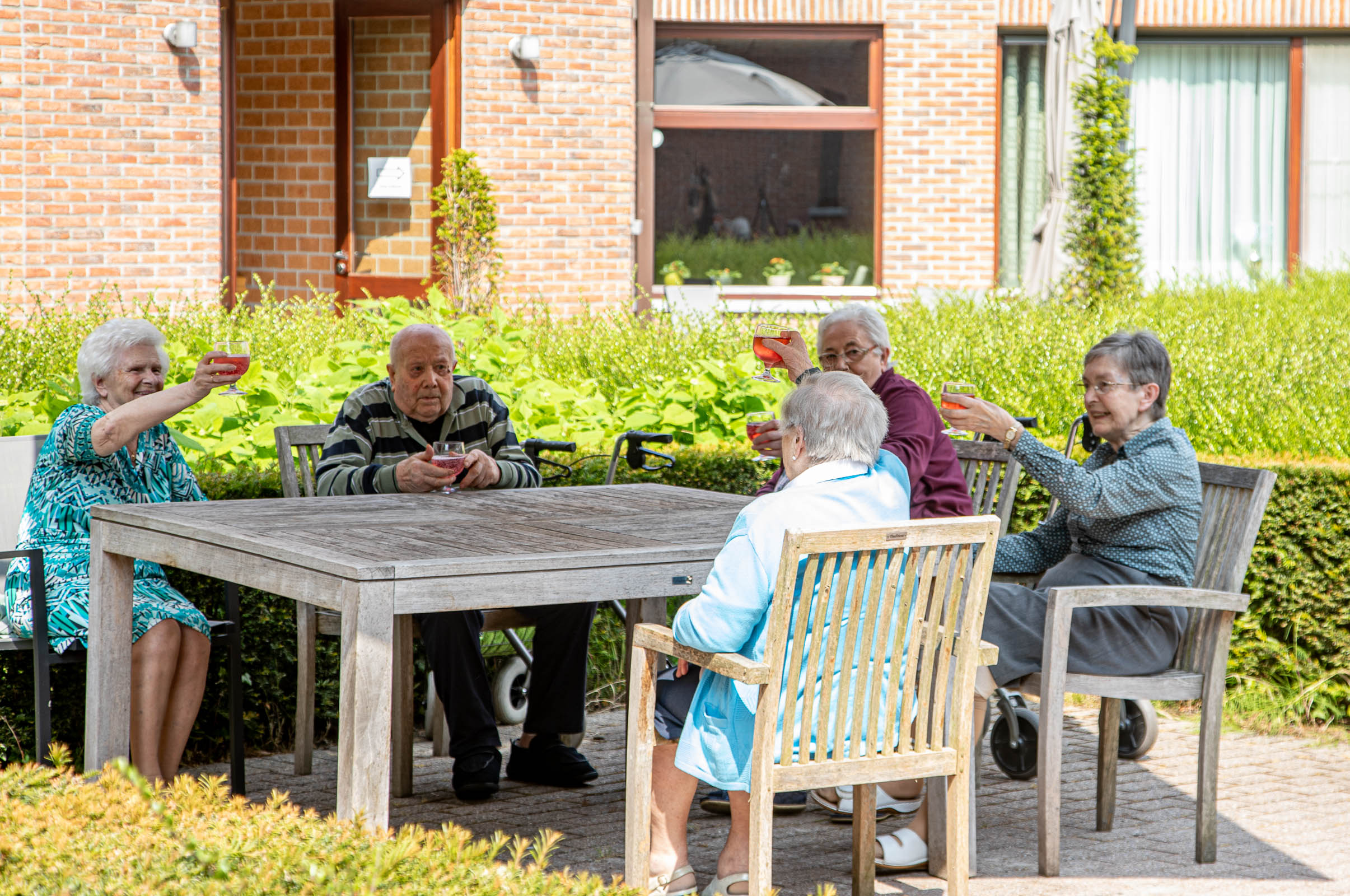Seniorenzorg Philippus Neri senior bewoners klinken de glazen op het zonnige terras van Huize Den Dries in Sinaai